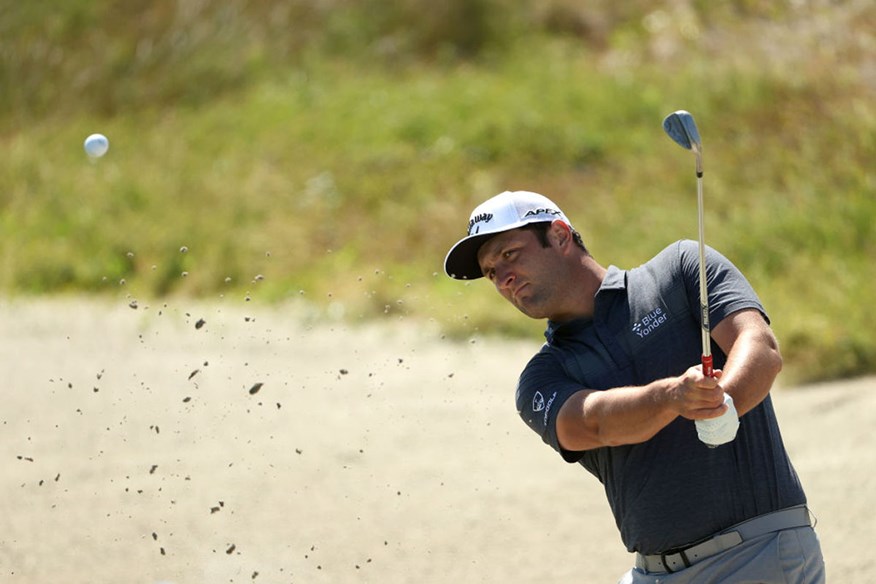 Jon Rahm plays a shot from a bunker.